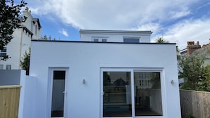 A modern white house with a flat roof, large sliding glass doors, and a dark wooden deck. - James' Place (Falmouth)