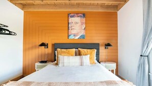 Ein Schlafzimmer mit einer Wand aus Holzpaneelen, einem Bett mit weißer Bettwäsche und zwei Kissen, zwei Nachttischen mit Lampen und einem Poster an der Wand.