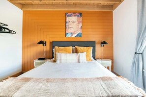 A bedroom with a wooden panel wall, a bed with white bedding and two pillows, two bedside tables with lamps, and a poster on the wall.