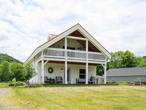 A two-story house with a balcony, a porch with seating, and a wreath on the door.