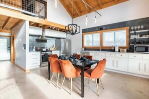 A modern kitchen with white cabinets, a black dining table, and orange chairs.