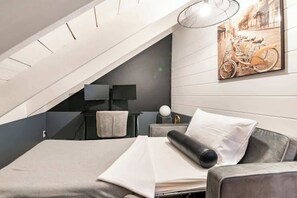 Ein modernes Schlafzimmer mit schrägem Dach, einem Bett mit grauem Kopfteil, einem Nachttisch mit Lampe sowie einem Wandbild mit Fahrrädern.