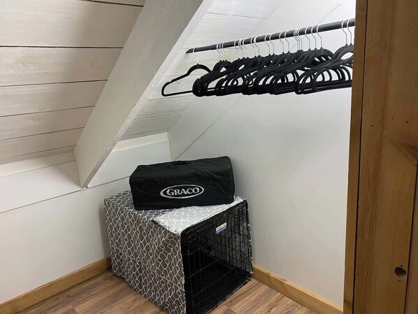 A corner of a room with a wooden floor, a black storage unit with a patterned cover, and a black coat hanging on a rack.