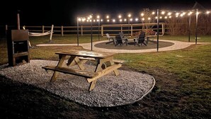 Ein Außenbereich mit einer Holzterrasse, einem Picknicktisch und Stühlen, umgeben von einem Kiesweg und einem Holenzaun.