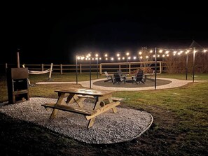 An outdoor patio area with a wooden picnic table and chairs, surrounded by a gravel path and a wooden fence.