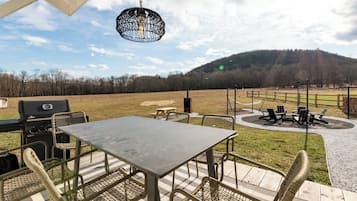Une terrasse extérieure avec une table et des chaises, un barbecue et un luminaire suspendu.