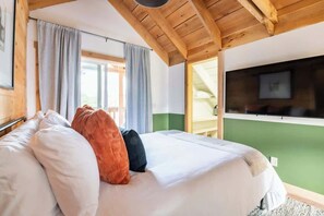 A bedroom with a large bed, wooden ceiling beams, a green wall, and a TV mounted on the wall. - The Bar(n)- Cozy chalet with hot tub and campfire (Brooktondale)