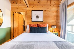 A wooden-paneled bedroom with a bed, a framed picture on the wall, and a window with curtains.