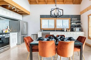 A modern kitchen with a dining area, featuring a large window, stainless steel appliances, and orange chairs.