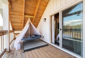 A wooden deck with a hanging canopy bed, a sliding glass door, and a view of the outdoors.