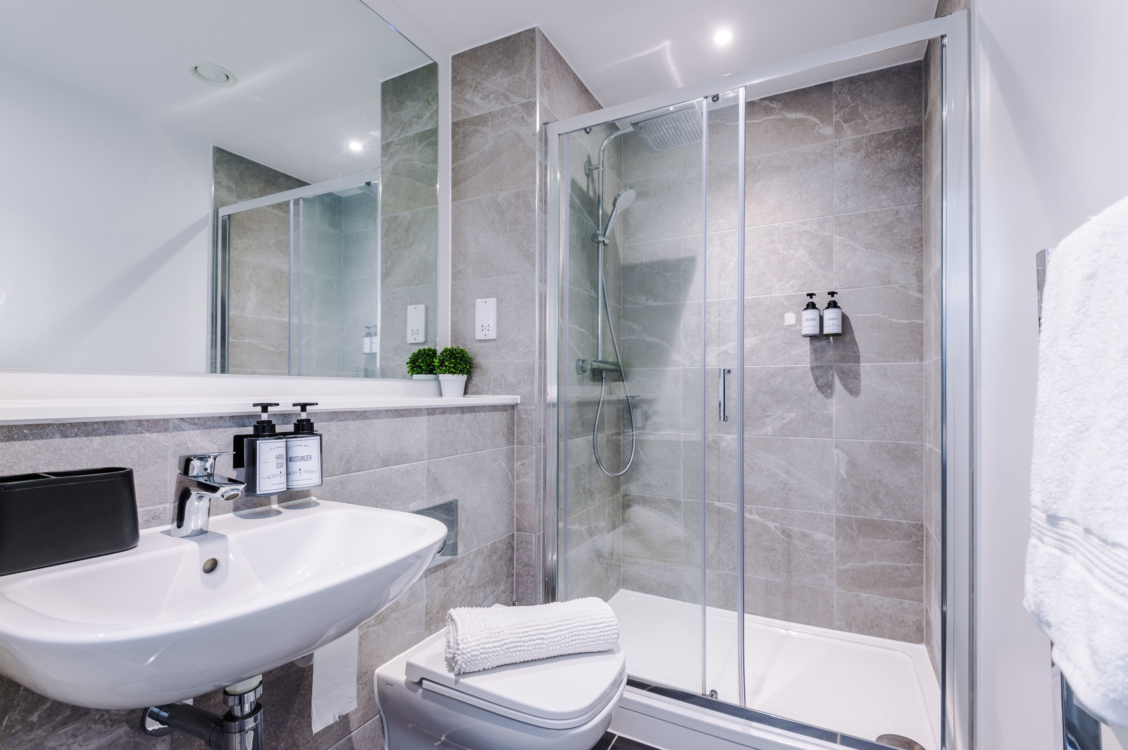 A modern bathroom with a glass-enclosed shower, a white sink, and a toilet.