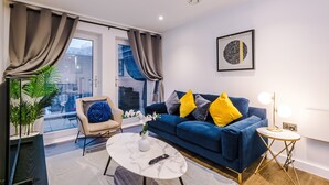 A modern living room with a blue sofa, a round coffee table, a chair with a blue pillow, and a potted plant. - Impeccable 2-bed Apartment in Salford (Salford)