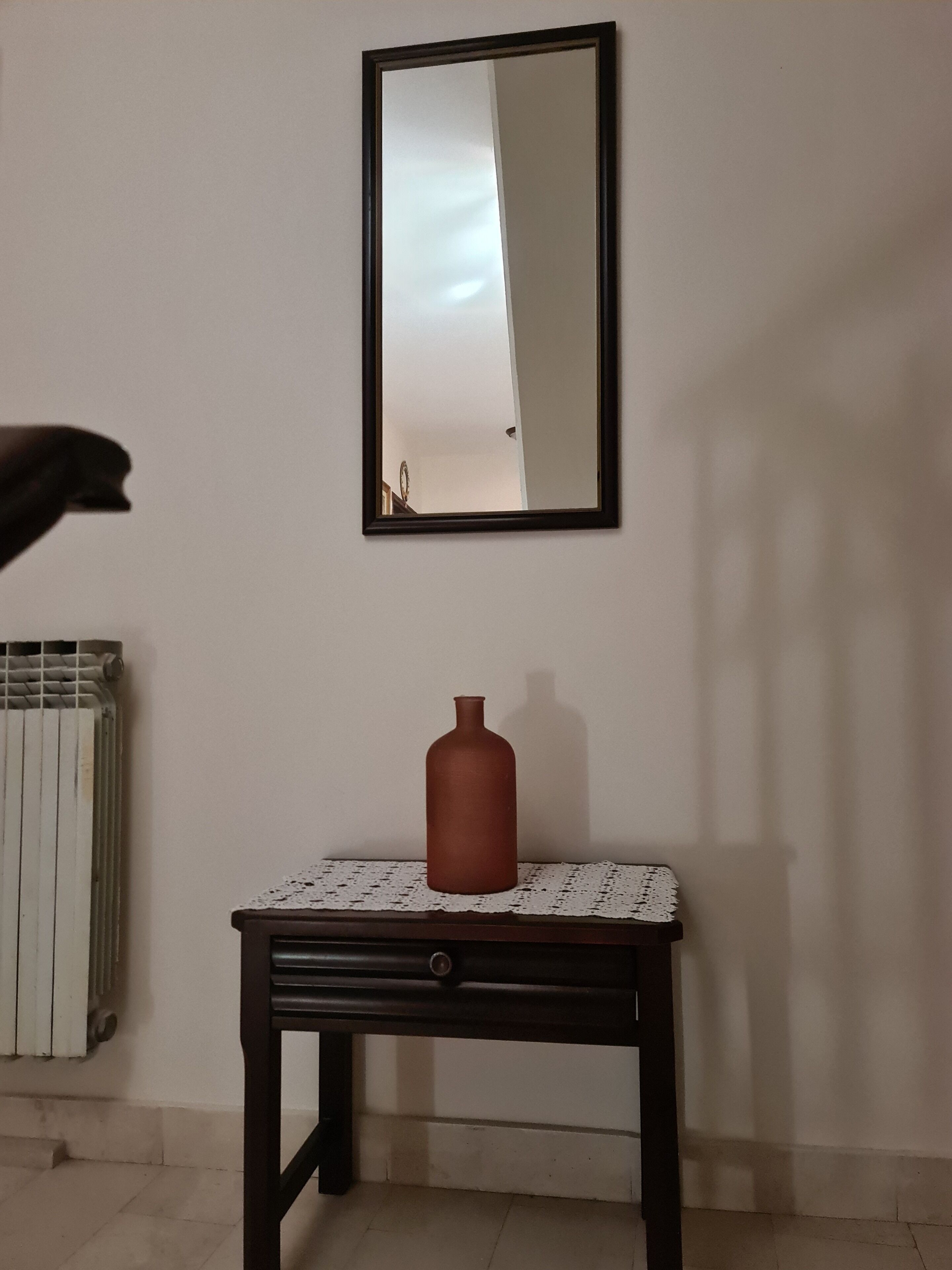 Une pièce avec un radiateur, une table sur laquelle se trouve un vase, et un miroir accroché au mur.