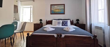 A bedroom with a wooden bed, a painting on the wall, and a view of the sea through the window.