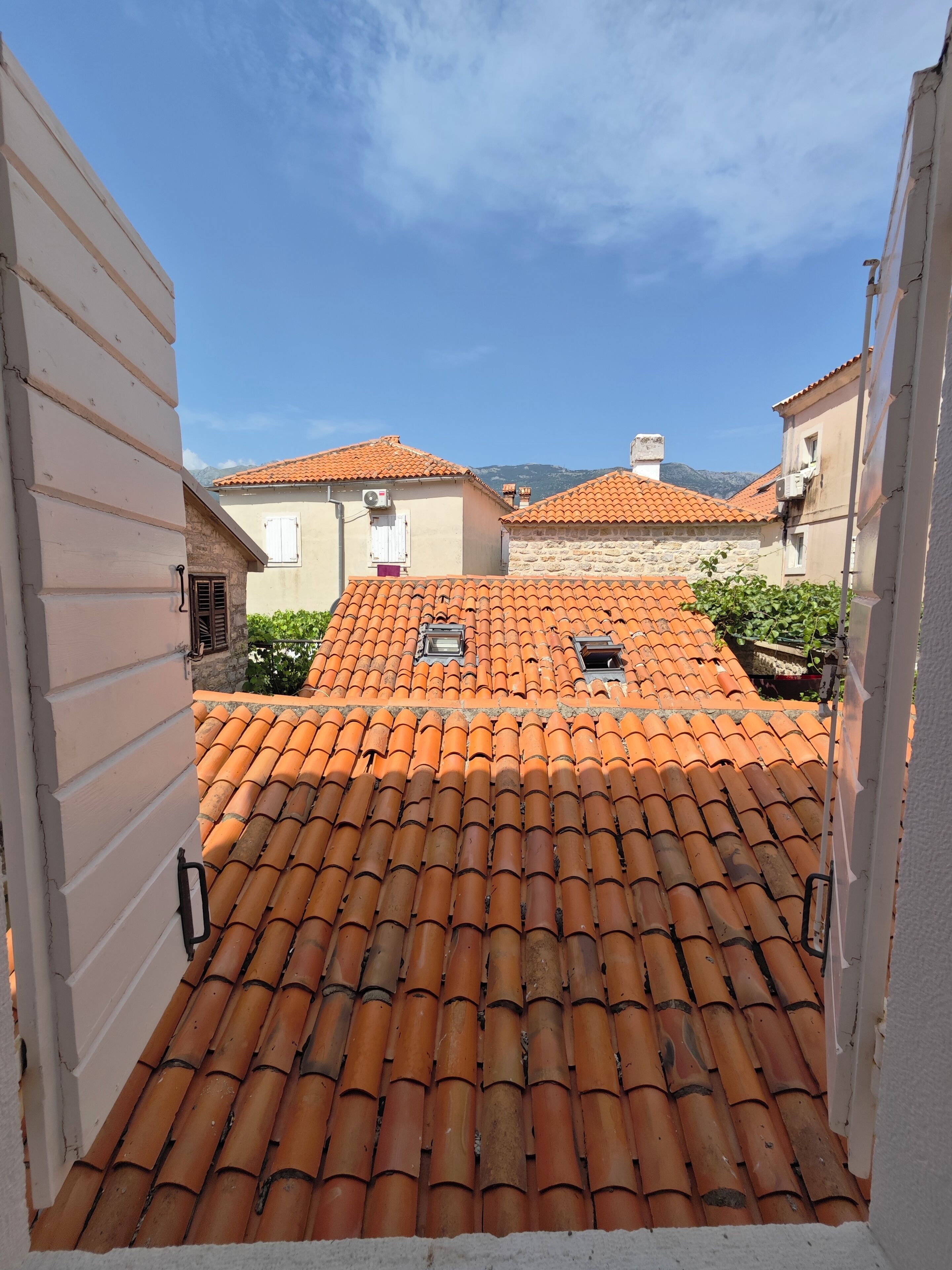 Blick auf ein mit Terrakotta gedecktes Dach durch einen schmalen Gang zwischen Gebäuden.