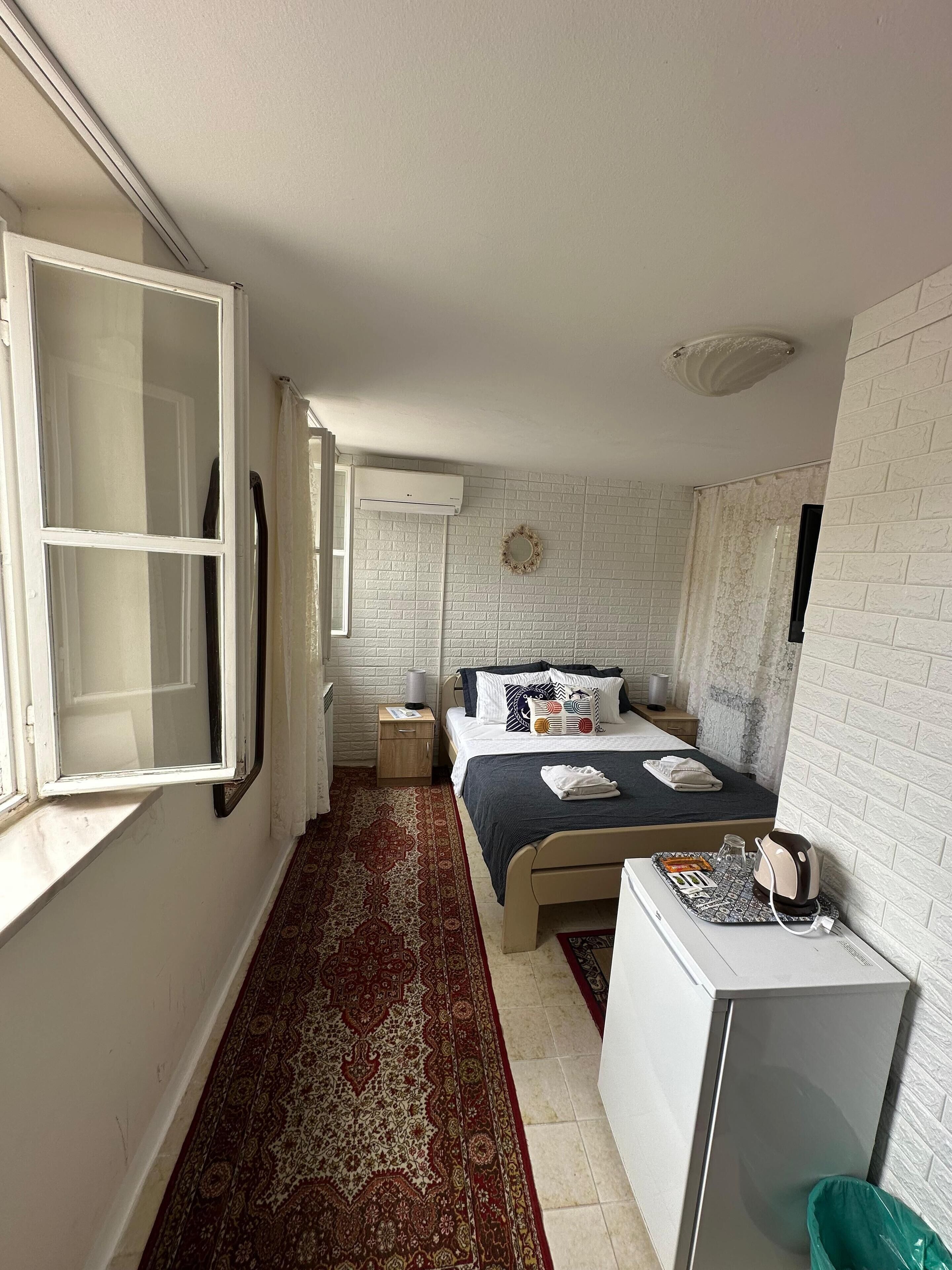 Una habitación de hotel compacta con cama, mesita de noche y una pequeña kitchenette.