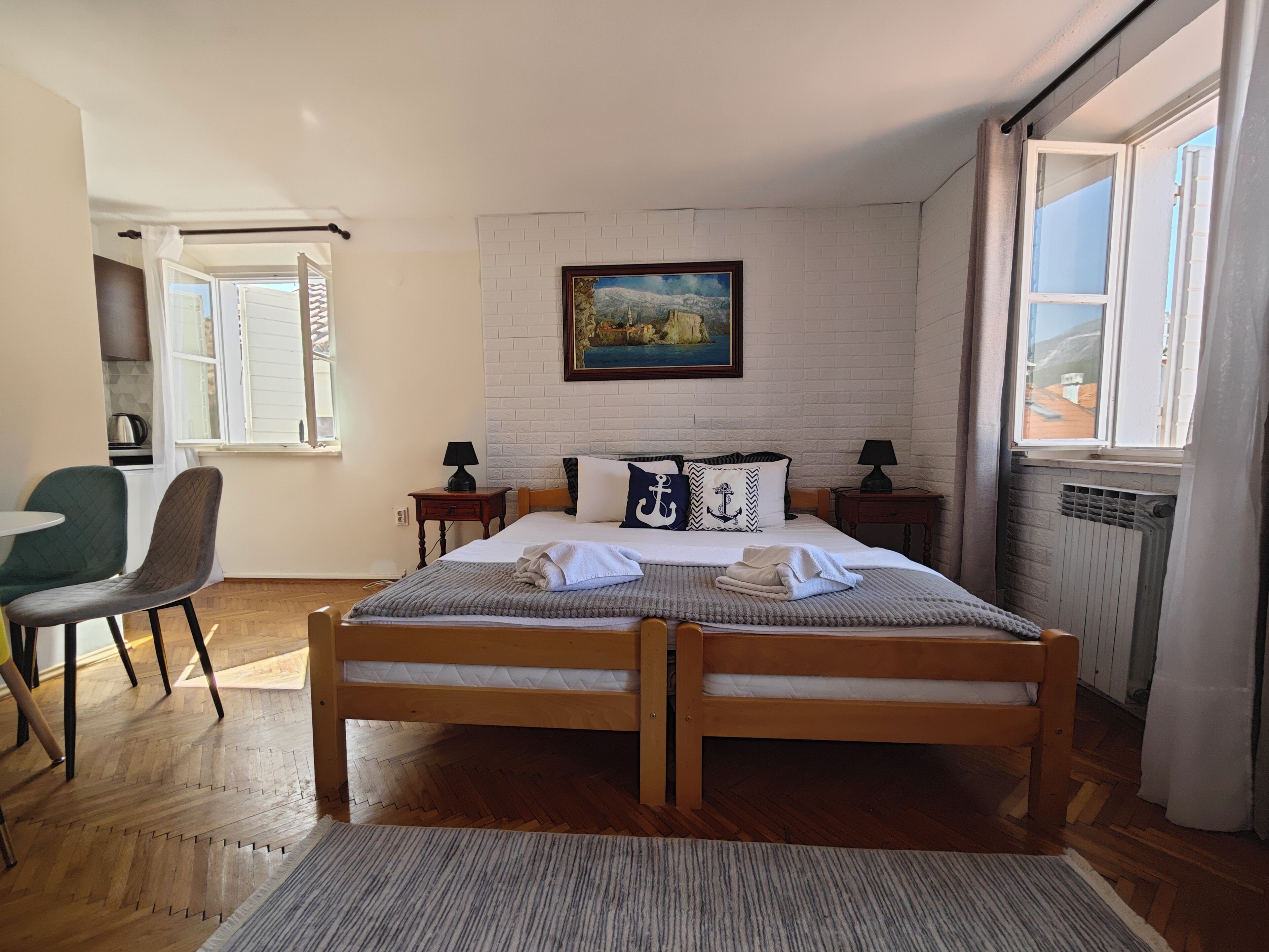 A bedroom with a double bed, a painting on the wall, a window with curtains, and a radiator.
