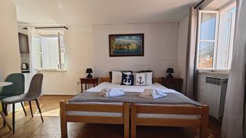 A bedroom with a double bed, a painting on the wall, a window with curtains, and a radiator.