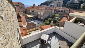Eine Dachterrasse mit Tisch und Stühlen, mit Blick auf eine historische Stadt mit Häusern mit Terrakotta-Dächern und einer Hügelkulisse.