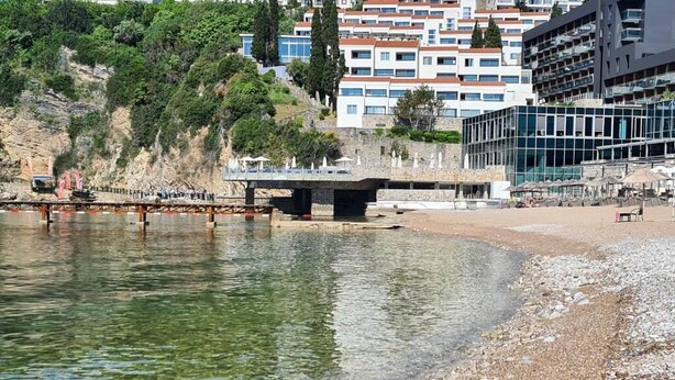 Ein Strand mit Kiesstrand, einer Brücke und Gebäuden im Hintergrund.