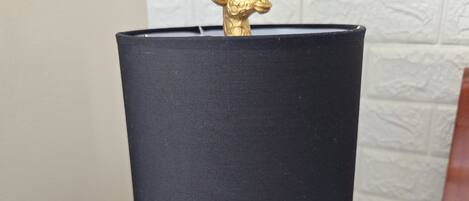 A table lamp with a black shade and a golden giraffe figurine on top, placed on a wooden nightstand.