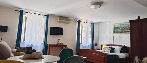 Habitación de hotel con cama, televisión, escritorio y zona de comedor con sillas y mesa.