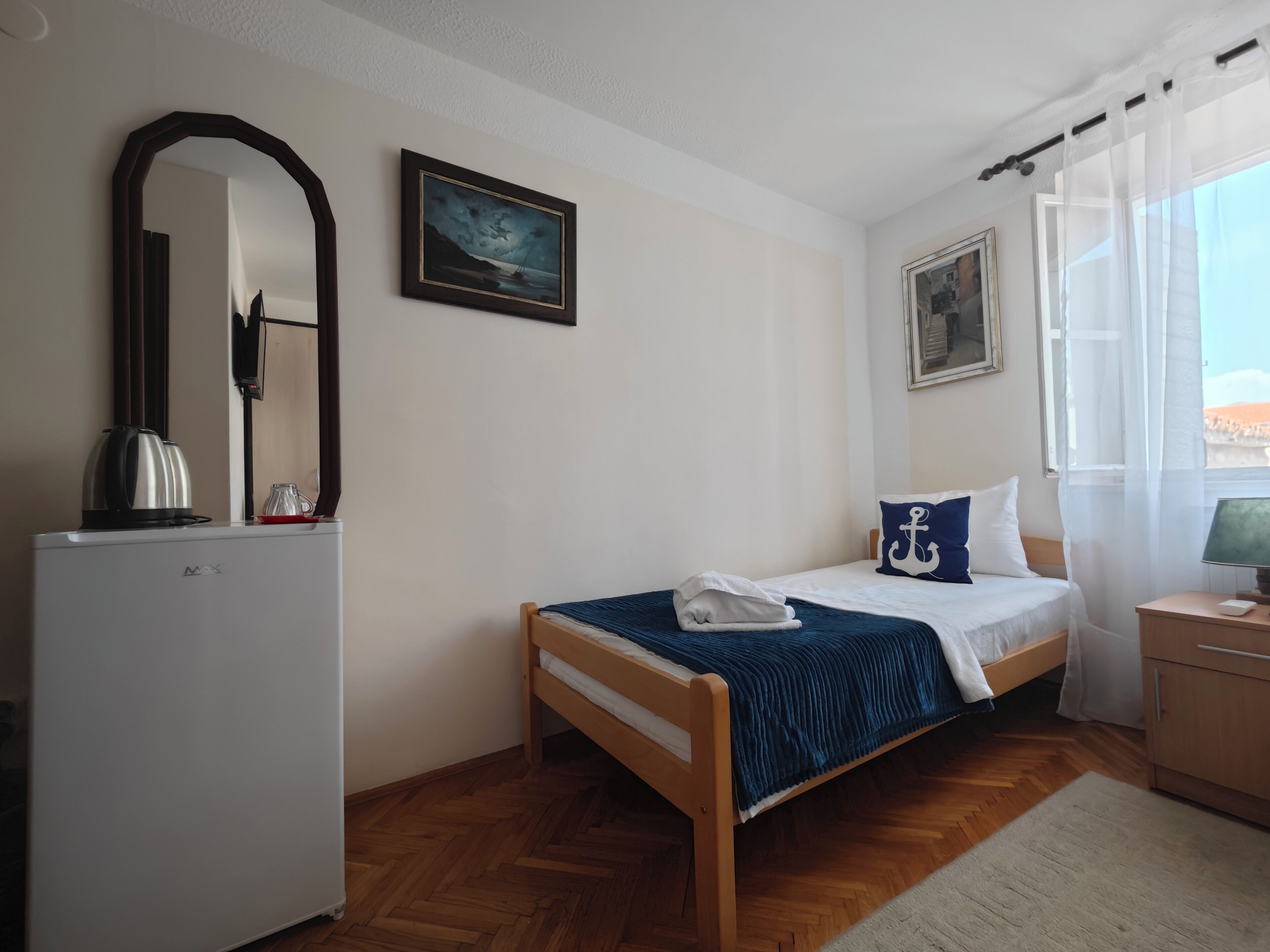 A bedroom with a bed, a desk, a mirror, and a picture on the wall.