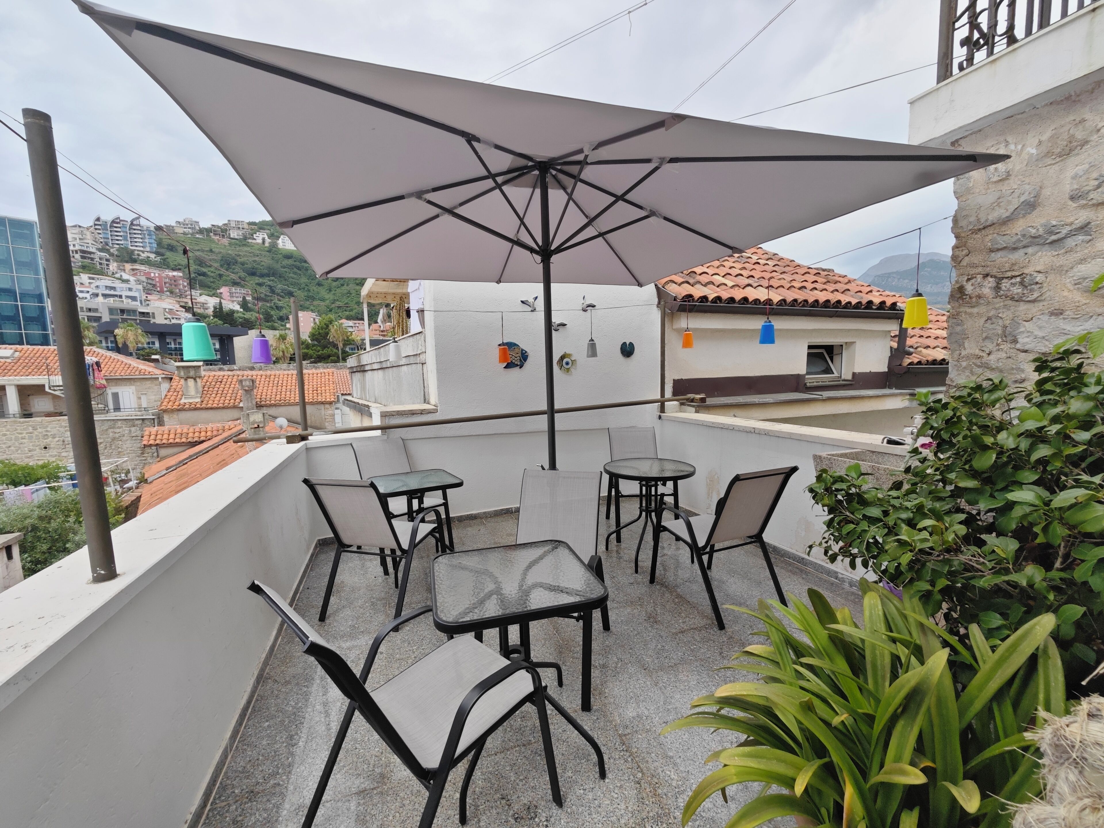 A rooftop terrace with a table and chairs, a large umbrella, and a view of the cityscape.