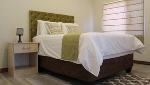 Quarto com cama, mesa de cabeceira, abajur e janela com persianas.