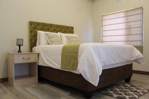 Un dormitorio con cama, mesita de noche, lámpara y ventana con persianas.