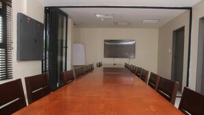 Uma sala de conferências com uma longa mesa de madeira, cadeiras, um quadro branco e uma tela de projetor.
