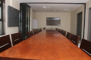 Una sala de conferencias con una larga mesa de madera, sillas, una pizarra y una pantalla para proyector.