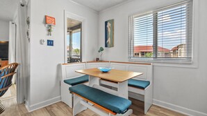 A kitchen with a wooden table and bench seating, a window with blinds, and a view of a red-roofed building outside. - Beautiful Coastal Retreat in North Myrtle Beach - Steps from the Ocean (North Myrtle Beach)