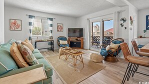 A spacious living room with a sofa, chairs, a TV, and a dining area. - Beautiful Coastal Retreat in North Myrtle Beach - Steps from the Ocean (North Myrtle Beach)