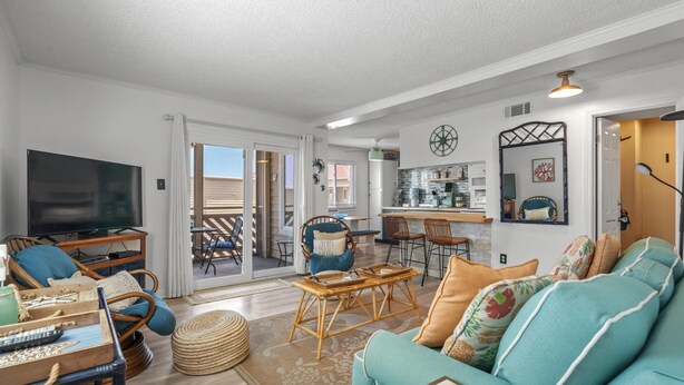 A spacious living room with a large TV, wicker furniture, and a teal sofa. - Beautiful Coastal Retreat in North Myrtle Beach - Steps from the Ocean (North Myrtle Beach)