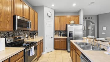 Una cocina moderna con armarios de madera, electrodomésticos de acero inoxidable, salpicadero de azulejos y piso de baldosas.
