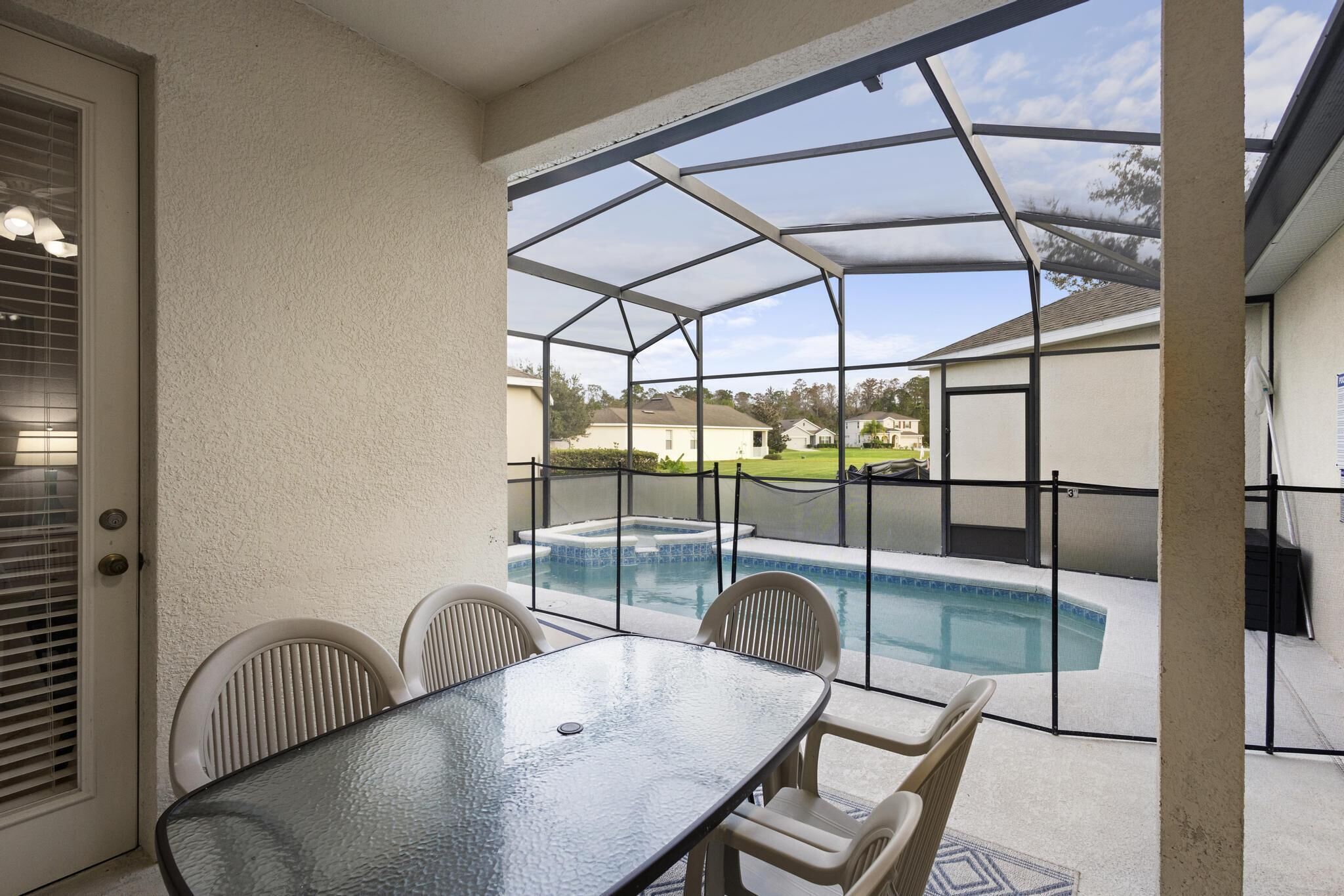 A covered patio with a glass enclosure, a pool, and a table with chairs.