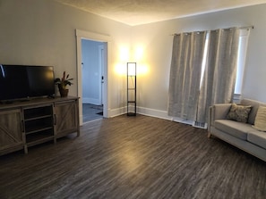 A living room with a flat-screen TV, a floor lamp, a sofa, and a door leading to another room. - Niles Spacious 2-Story Family & Work Haven (Niles)