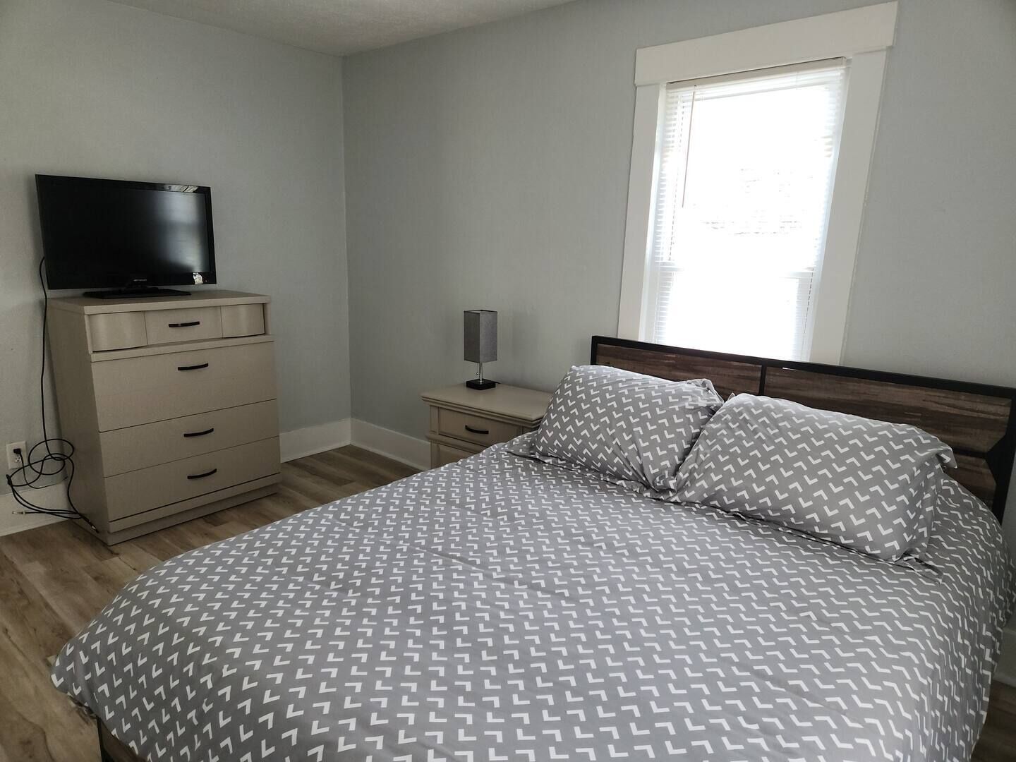 A bedroom with a bed, a dresser, a TV, and a window.