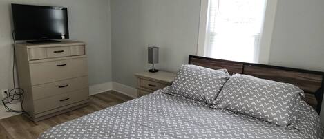 A bedroom with a bed, a dresser, a TV, and a window.