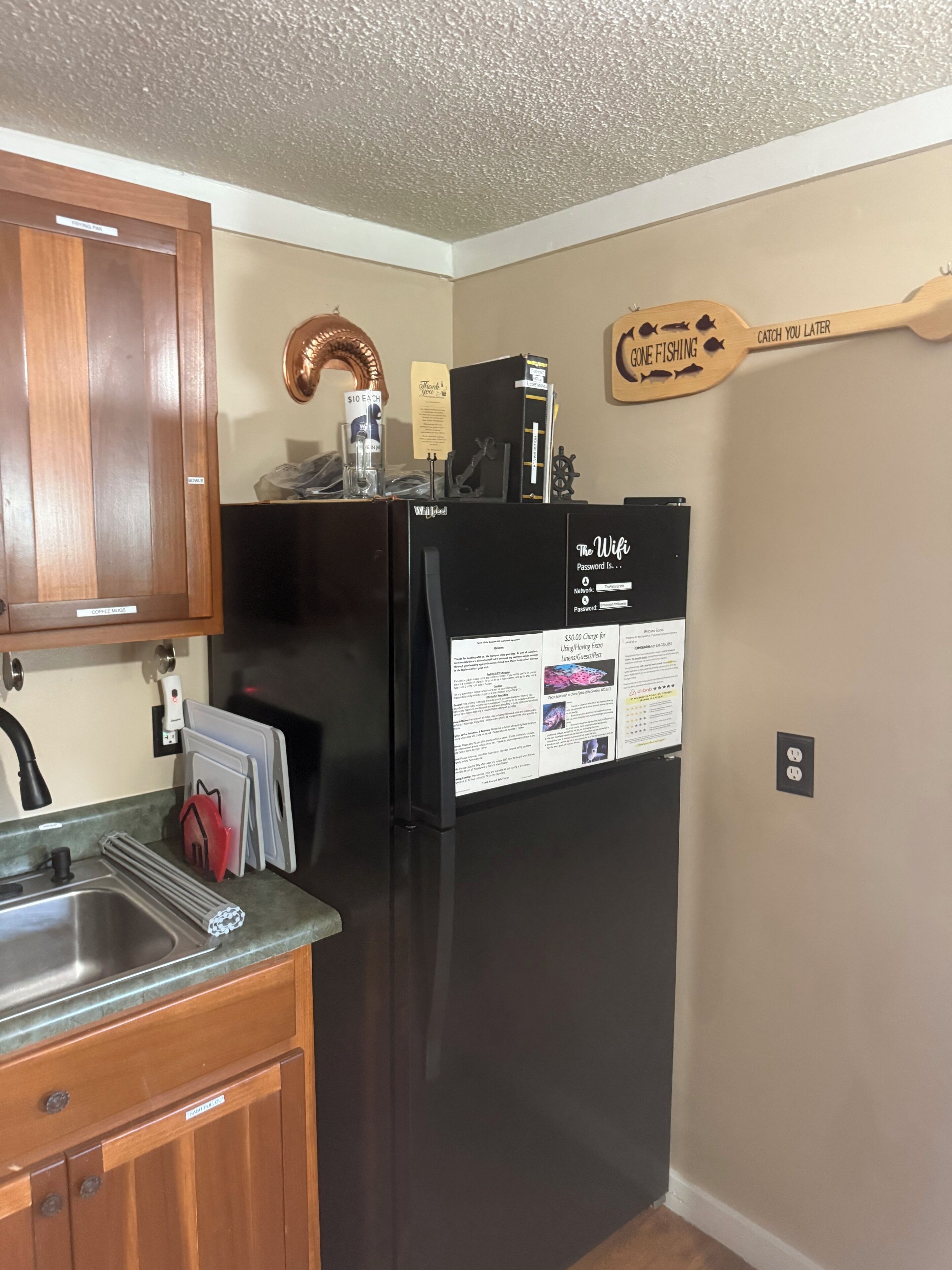 A kitchen with wooden cabinets, a black refrigerator, and a wooden sign on the wall.