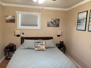 A bedroom with a bed, two bedside tables, a nightstand, a window with blinds, and wall art.