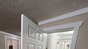 Pasillo que conduce a un baño con ducha, inodoro y lavamanos. A la izquierda hay una puerta y una escalera que sube a otra habitación.