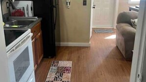 Cocina compacta con refrigerador, estufa y armarios. Un tapete estampado recorre el pasillo.