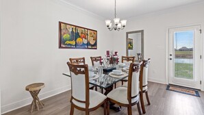 A dining room with a glass table, wooden chairs, a chandelier, and a painting on the wall.