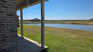 A covered outdoor area with a brick wall, a concrete floor, and a view of a body of water and distant buildings.