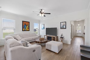 A spacious living room with a large sectional sofa, a flat-screen TV, and a ceiling fan.