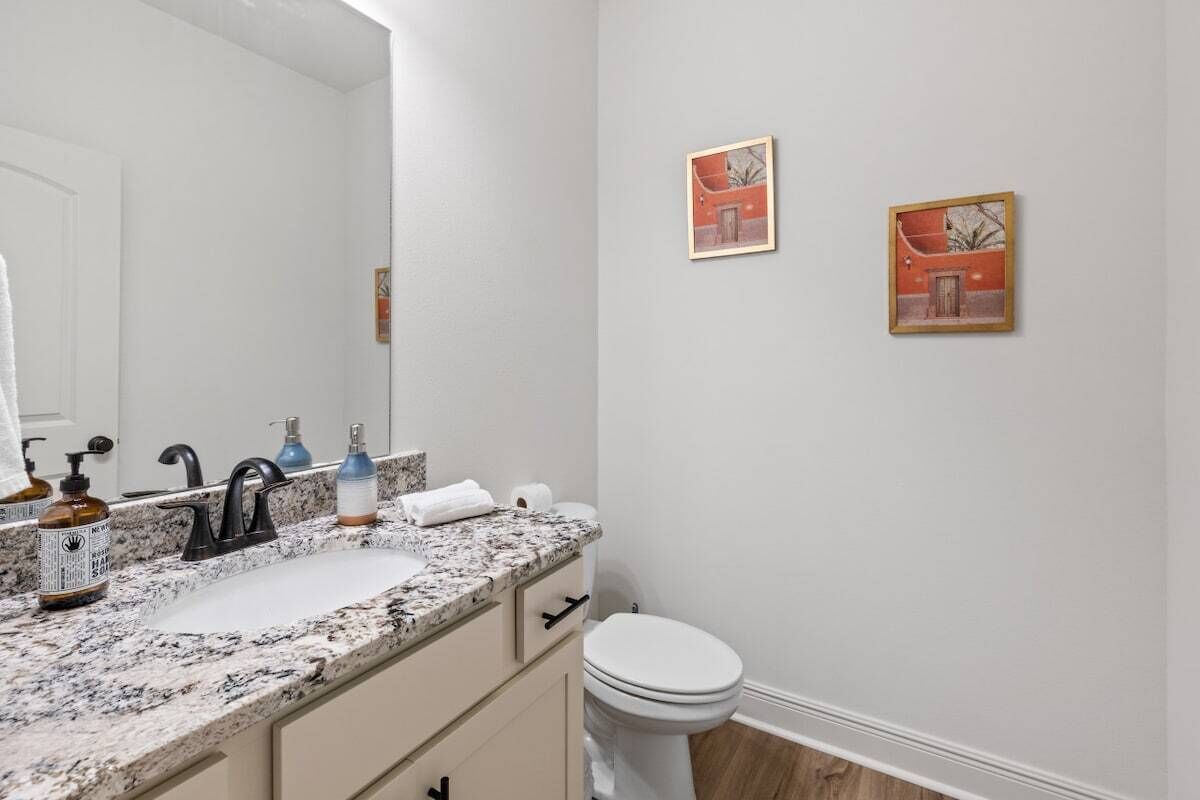 Un baño con un lavamanos blanco, grifo negro y un inodoro blanco. Hay dos cuadros en la pared.