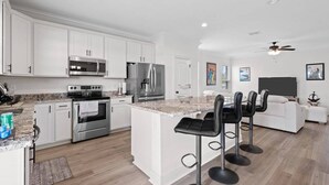 A modern kitchen with white cabinetry, stainless steel appliances, a granite countertop, and a bar area with stools.
