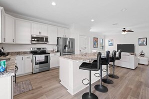Cocina moderna con armarios blancos, electrodomésticos de acero inoxidable, encimera de granito y una zona de bar con taburetes.